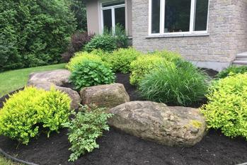 Boulders and shrubs in a front bed against a stone house